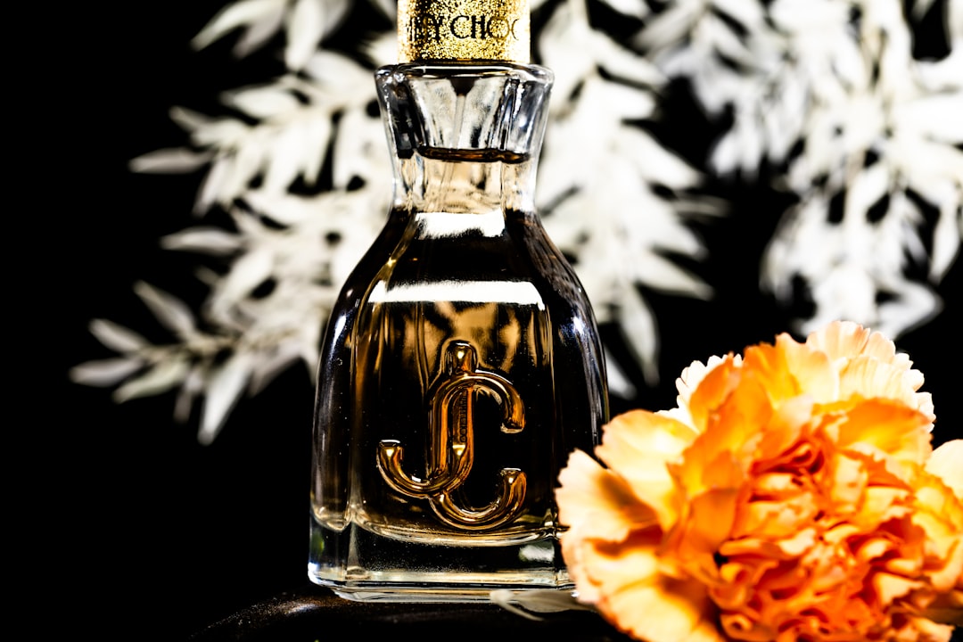 Perfume bottle with golden logo, white foliage, and orange flower.
