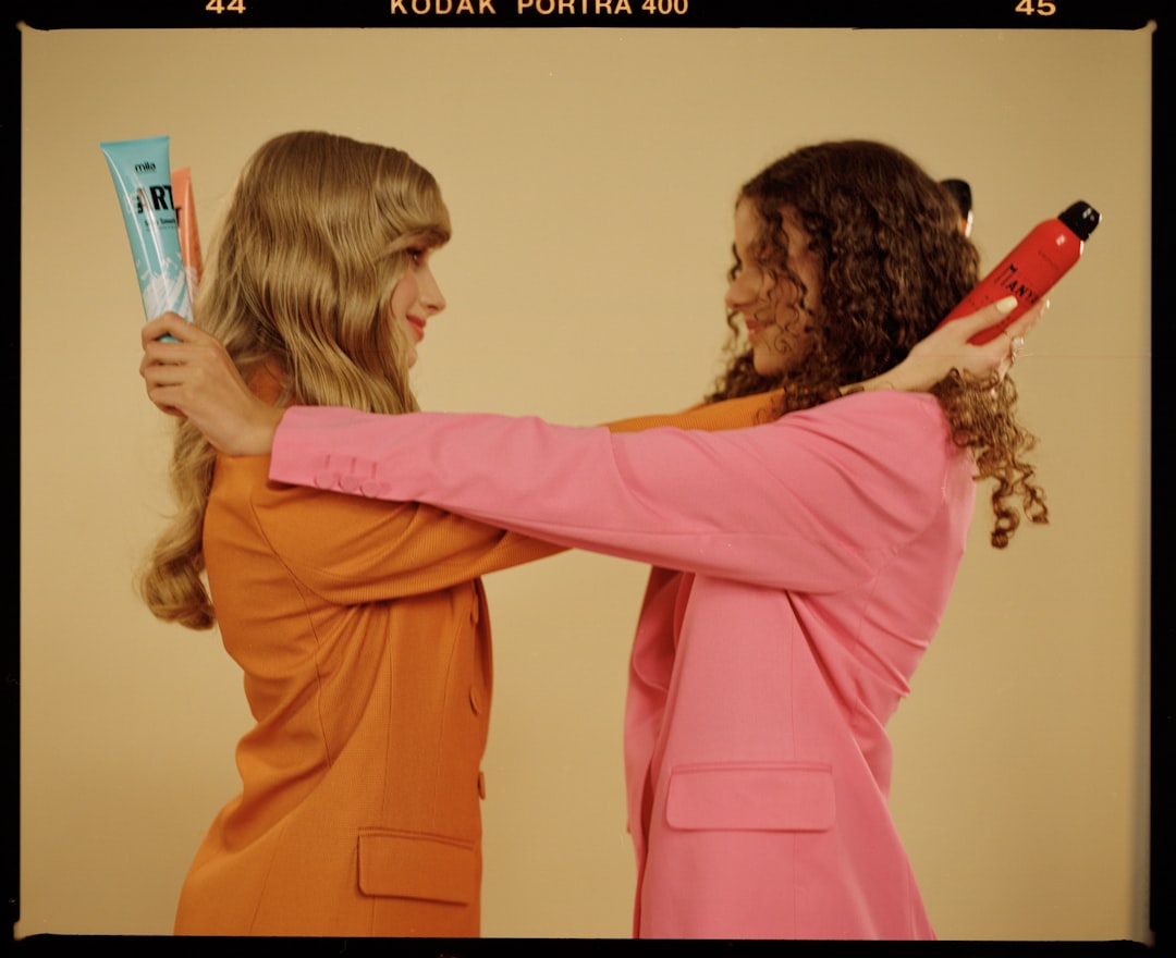 Two women in blazers exchanging beauty products.
