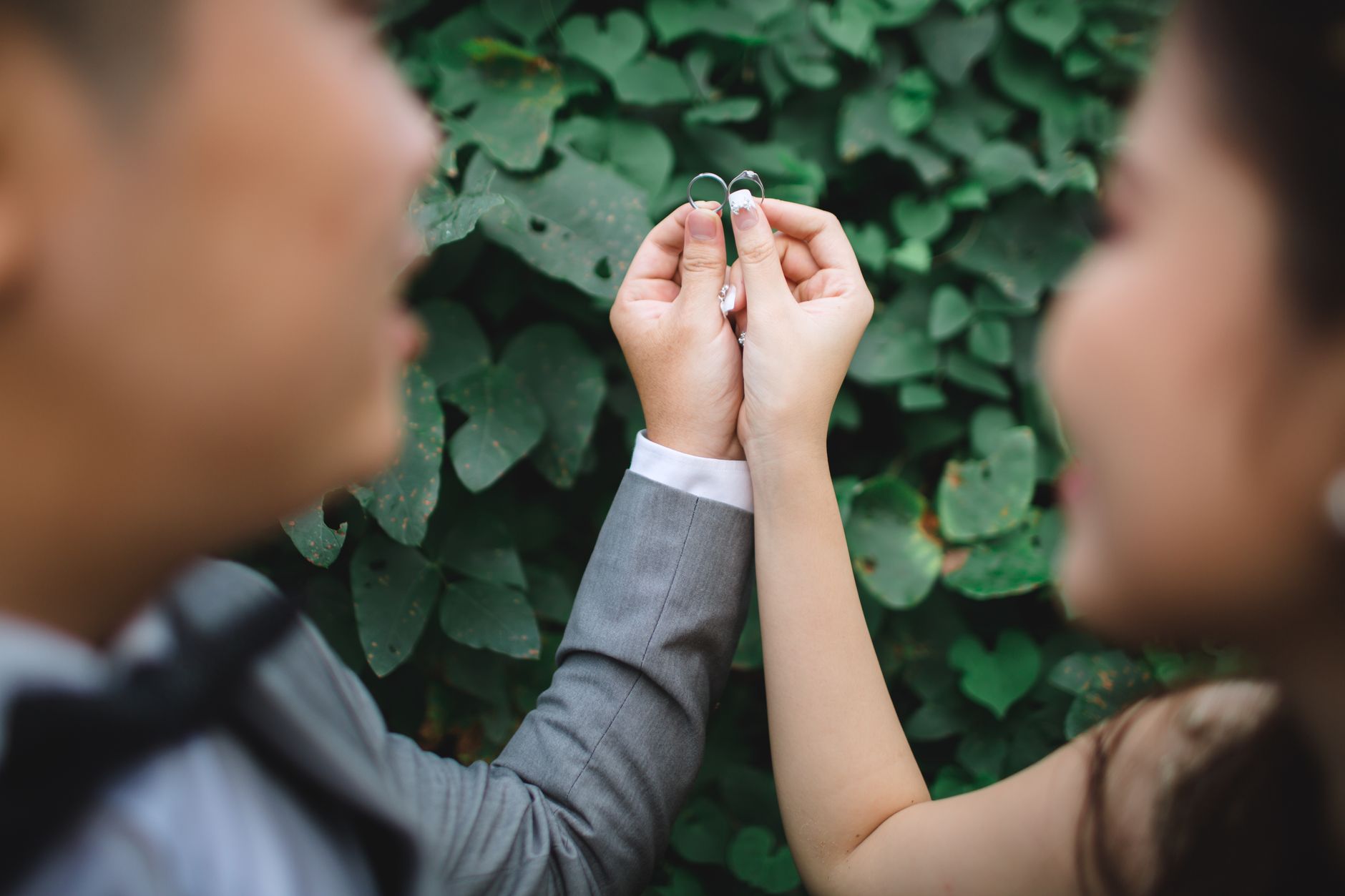Close-up of a couple holding wedding rings with lush green background, symbolizing love and unity.