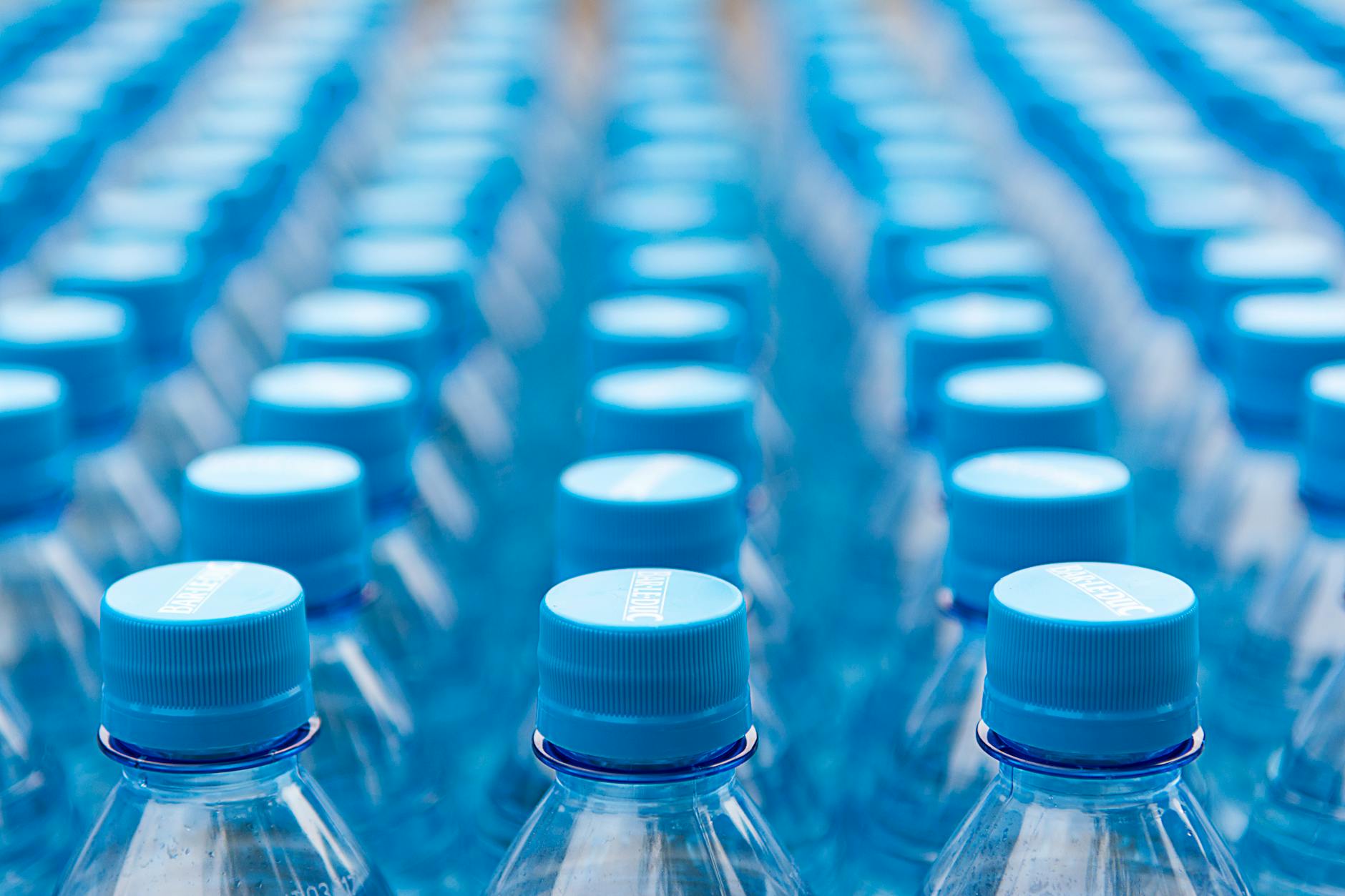 Array of blue plastic water bottles with caps arranged in a pattern. Ideal for recycling and packaging themes.