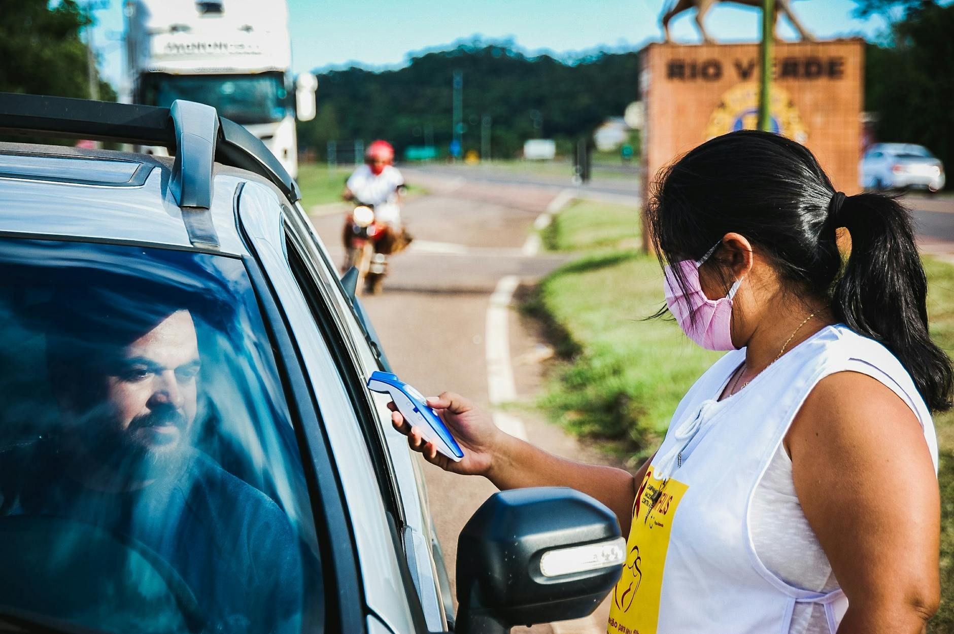 A woman checks a driver's temperature at a roadside checkpoint during COVID-19 pandemic.