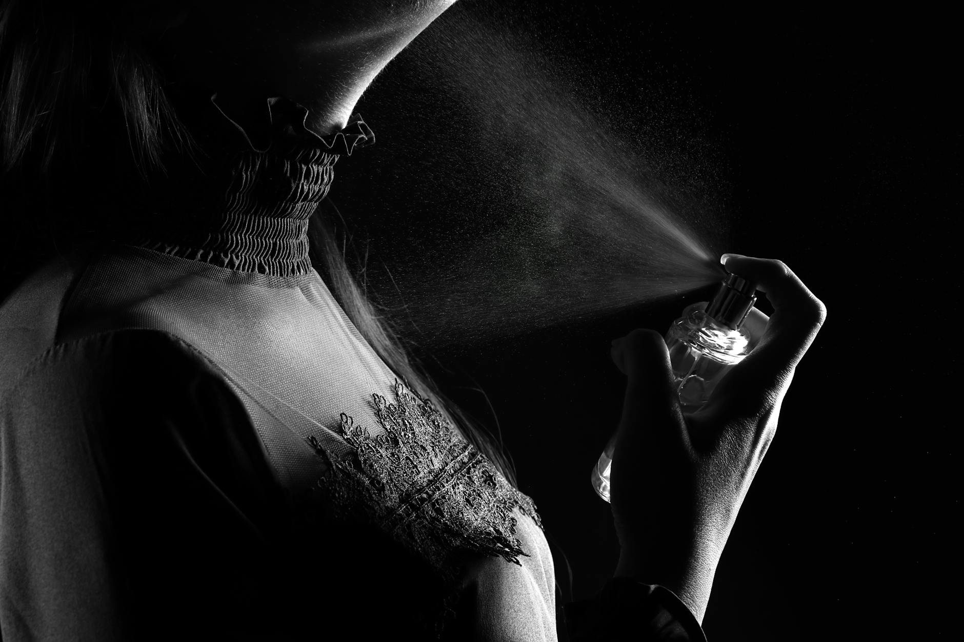 A stylish woman sprays perfume, captured in a dramatic black and white studio shot.