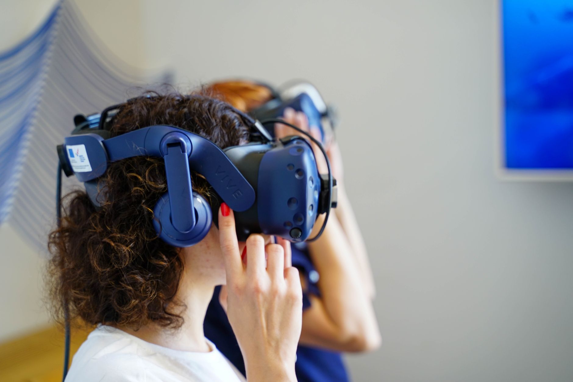 Two women using VR headsets, fully immersed in virtual reality technology indoors.
