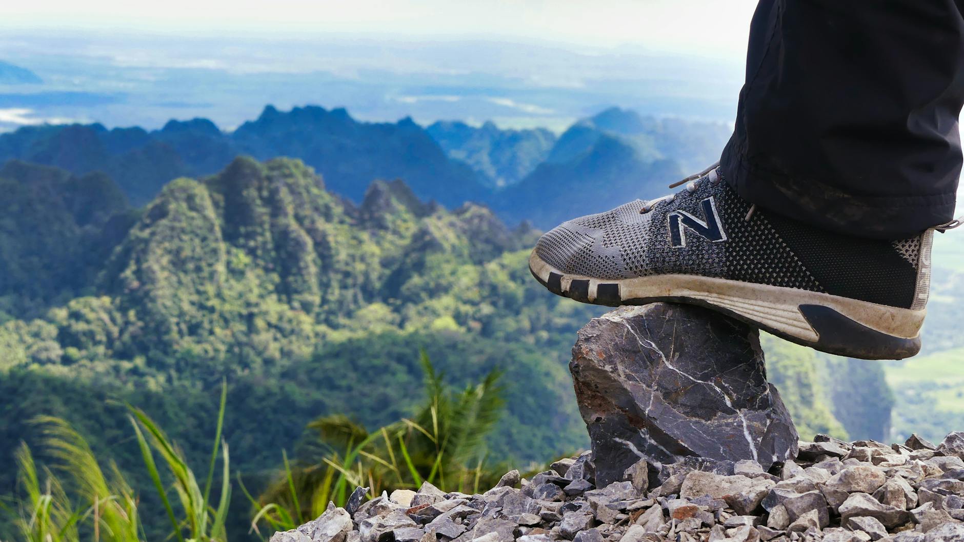 Foot in sneaker perched on rocks with Myanmar's limestone mountains in the background.