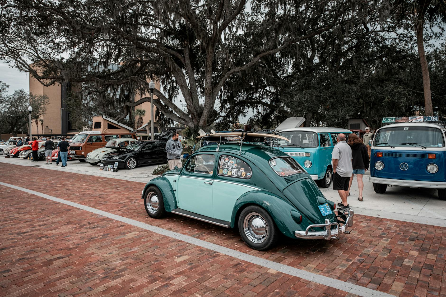 Classic Volkswagen Beetle with surfboard at a vintage car show outdoors.