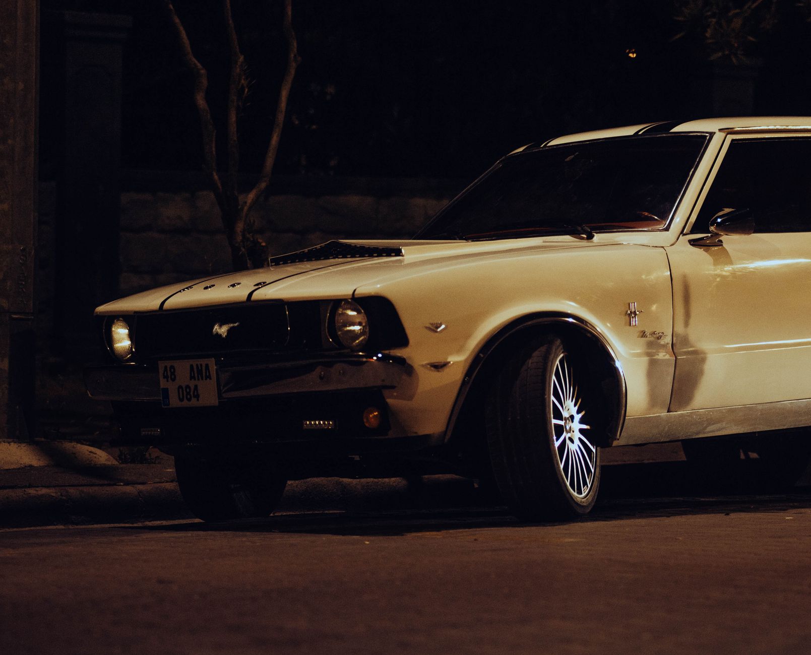 Vintage white Ford Mustang parked on dark city street, showcasing automotive nostalgia and retro style.