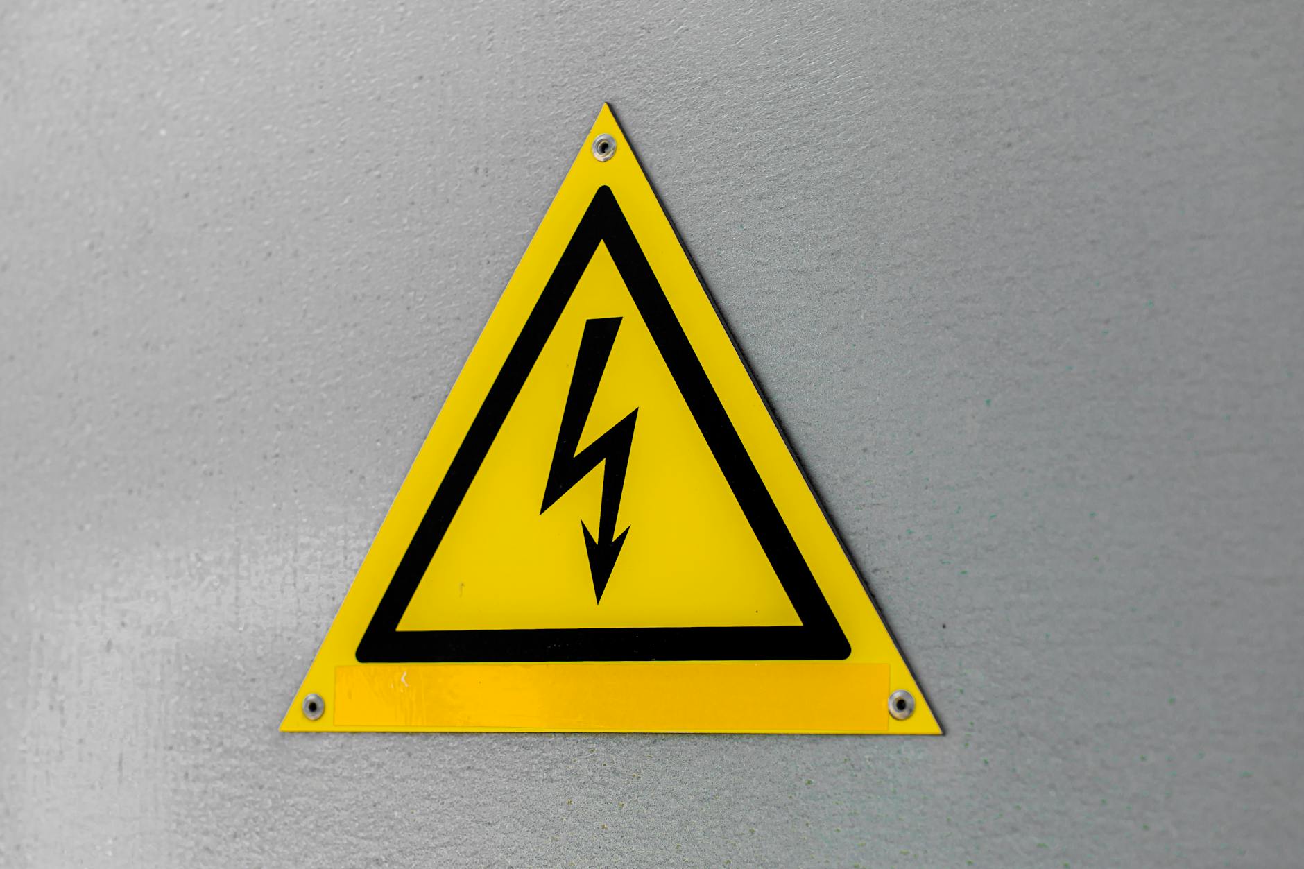 Close-up of a yellow high voltage warning sign mounted on a wall.