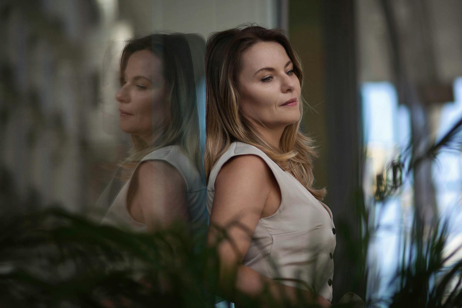 Elegant woman with long blonde hair leaning by a window with reflection.