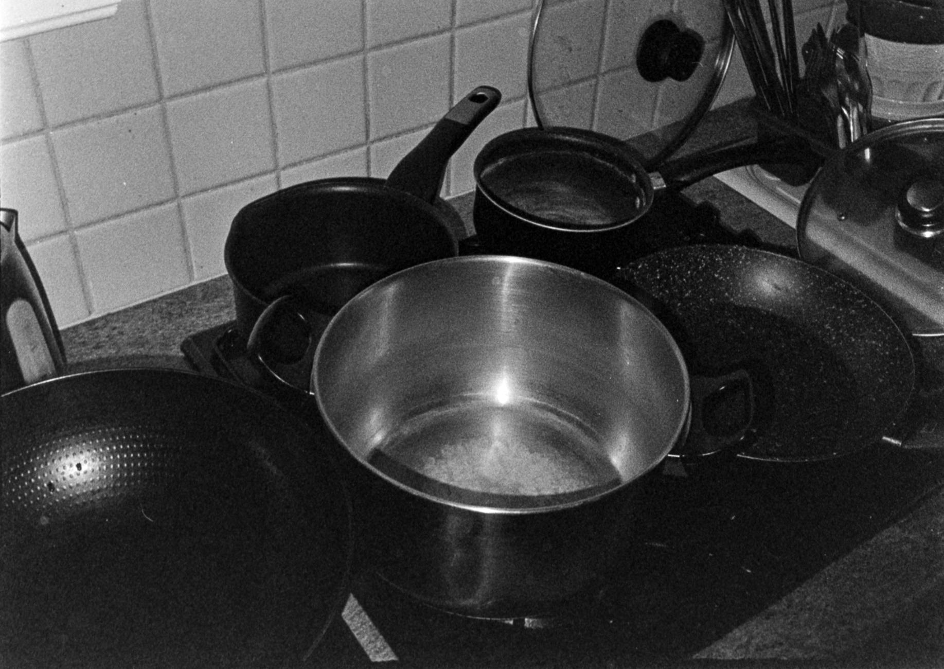A black and white still life of kitchen utensils and pots on the countertop.