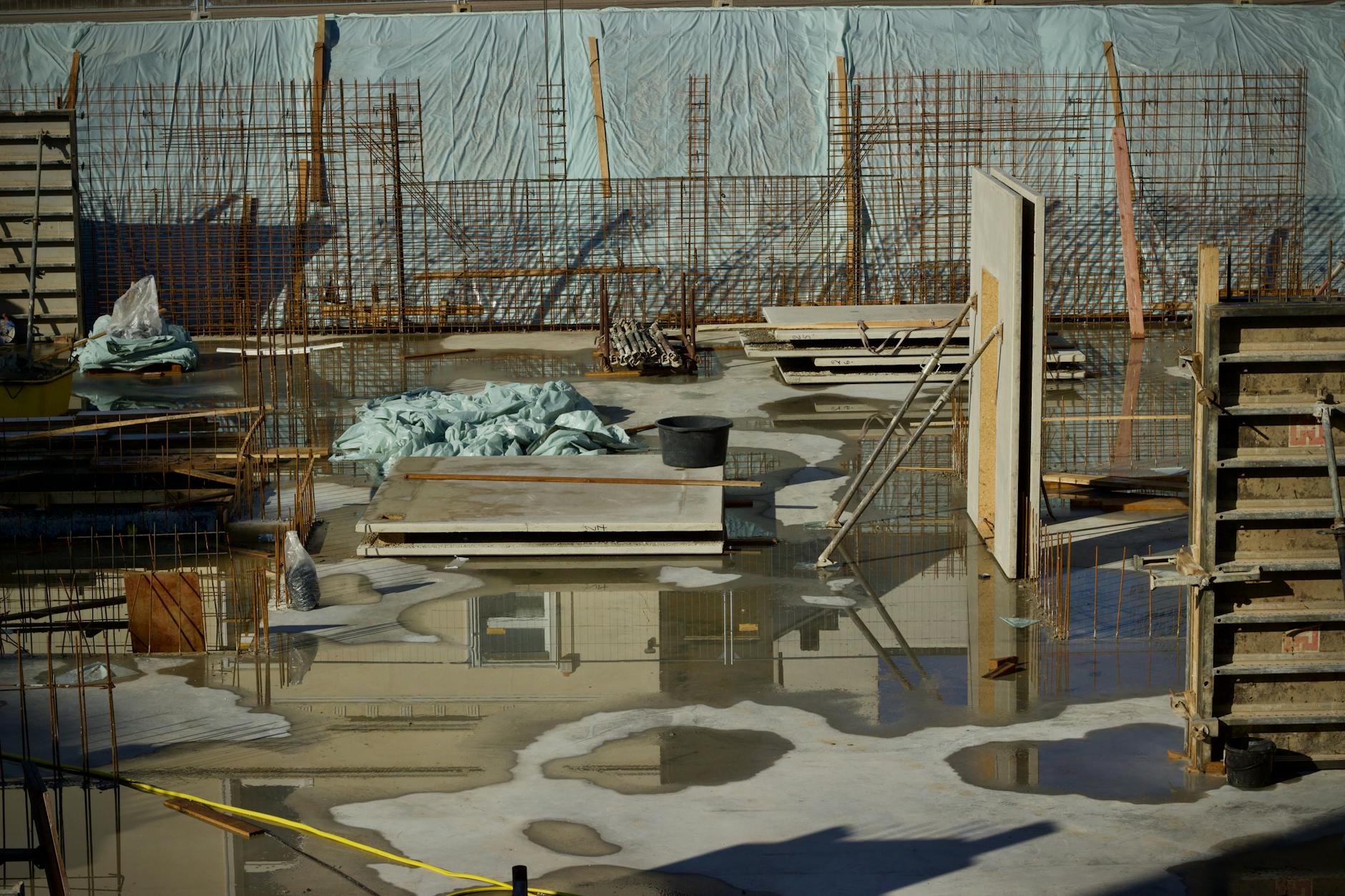 A flooded construction site with scattered materials and visible metal reinforcement.