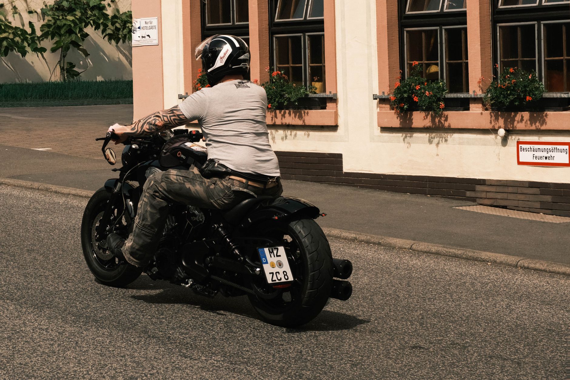 A motorcyclist rides past a traditional German building on a sunny day.