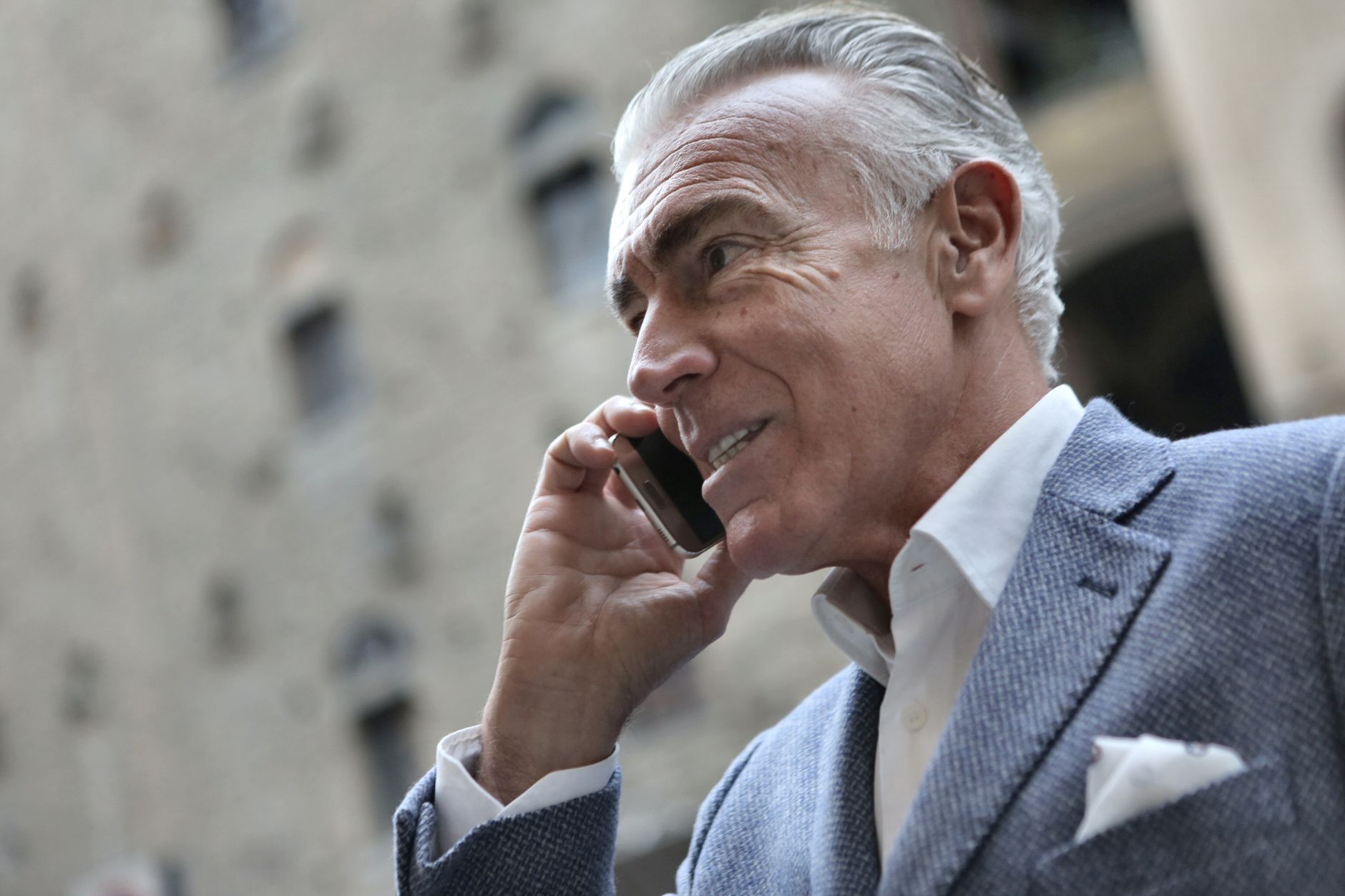 Confident senior man in a suit talking on his smartphone outdoors during the day.