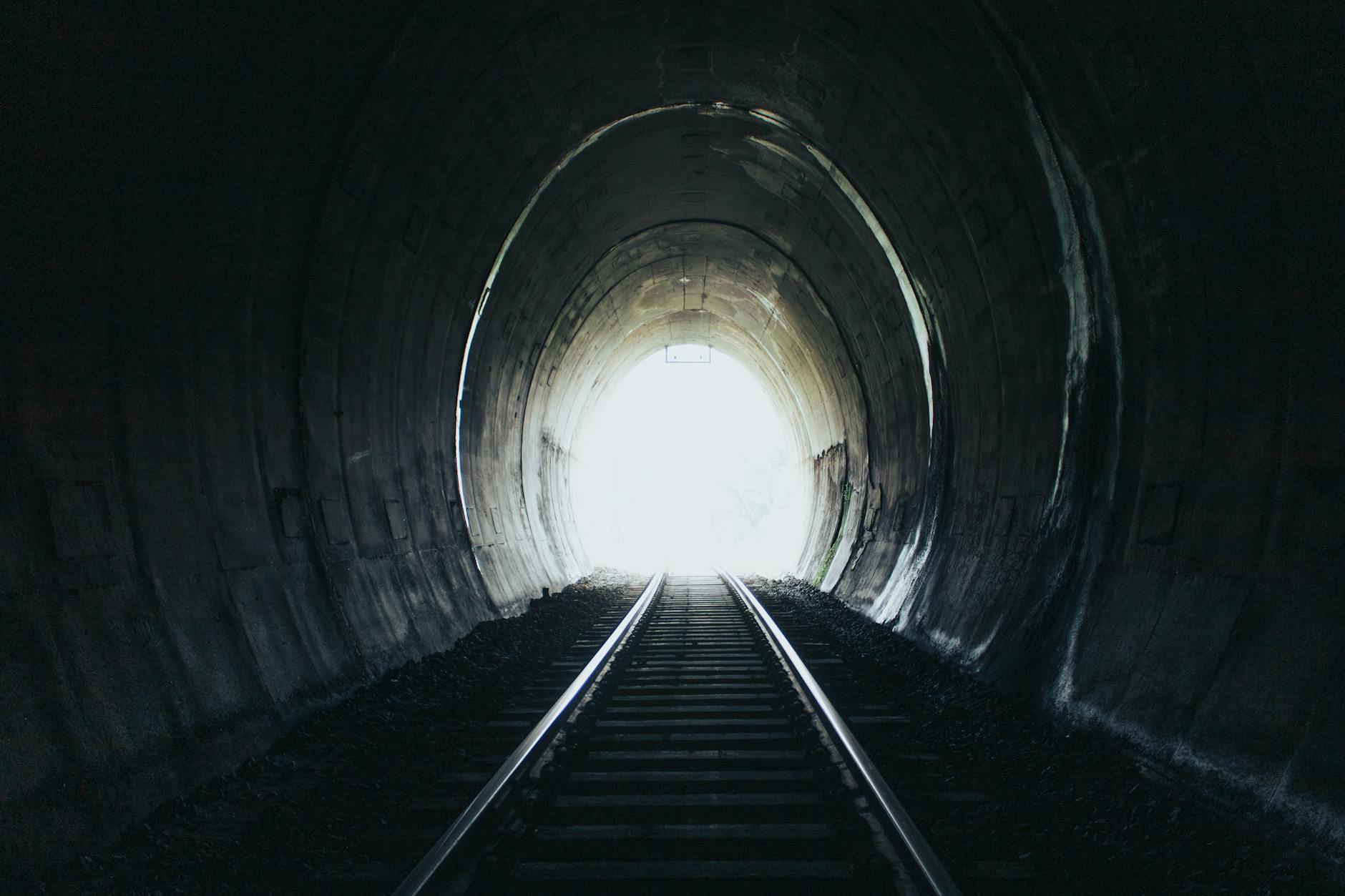 A captivating perspective of railroad tracks inside a dark tunnel leading towards bright light.