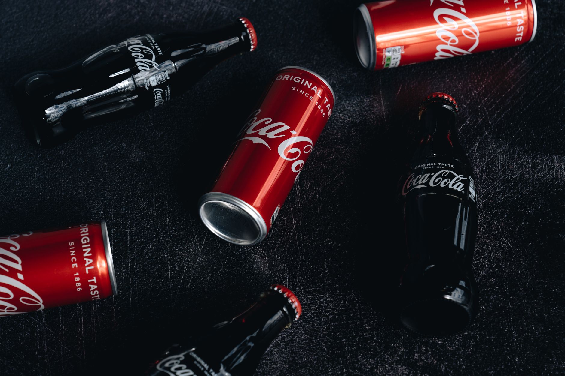 Coca-Cola cans and bottles artfully arranged on a textured dark surface.