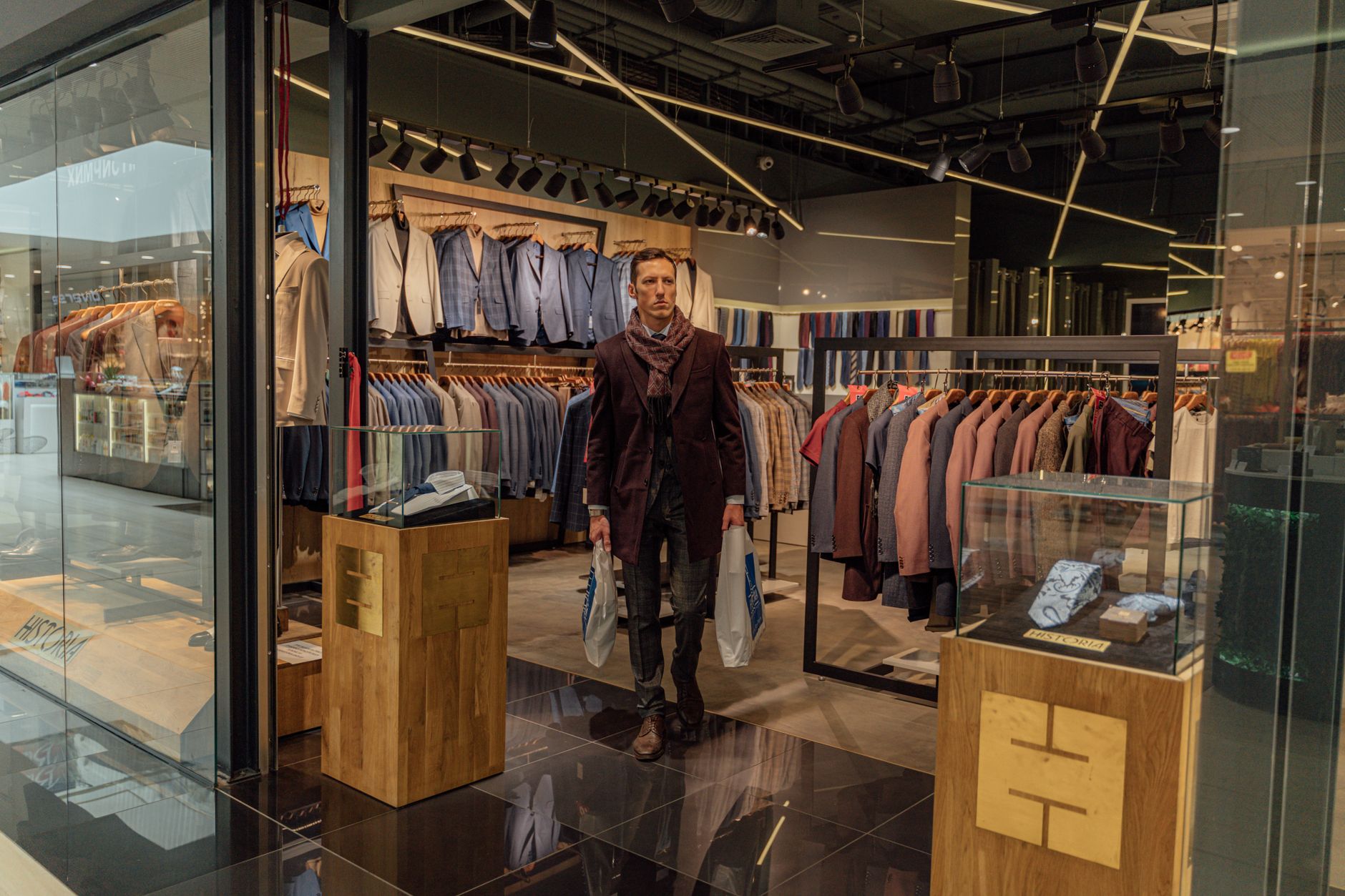 Man in a modern clothing store holding shopping bags, showcasing fashion options.