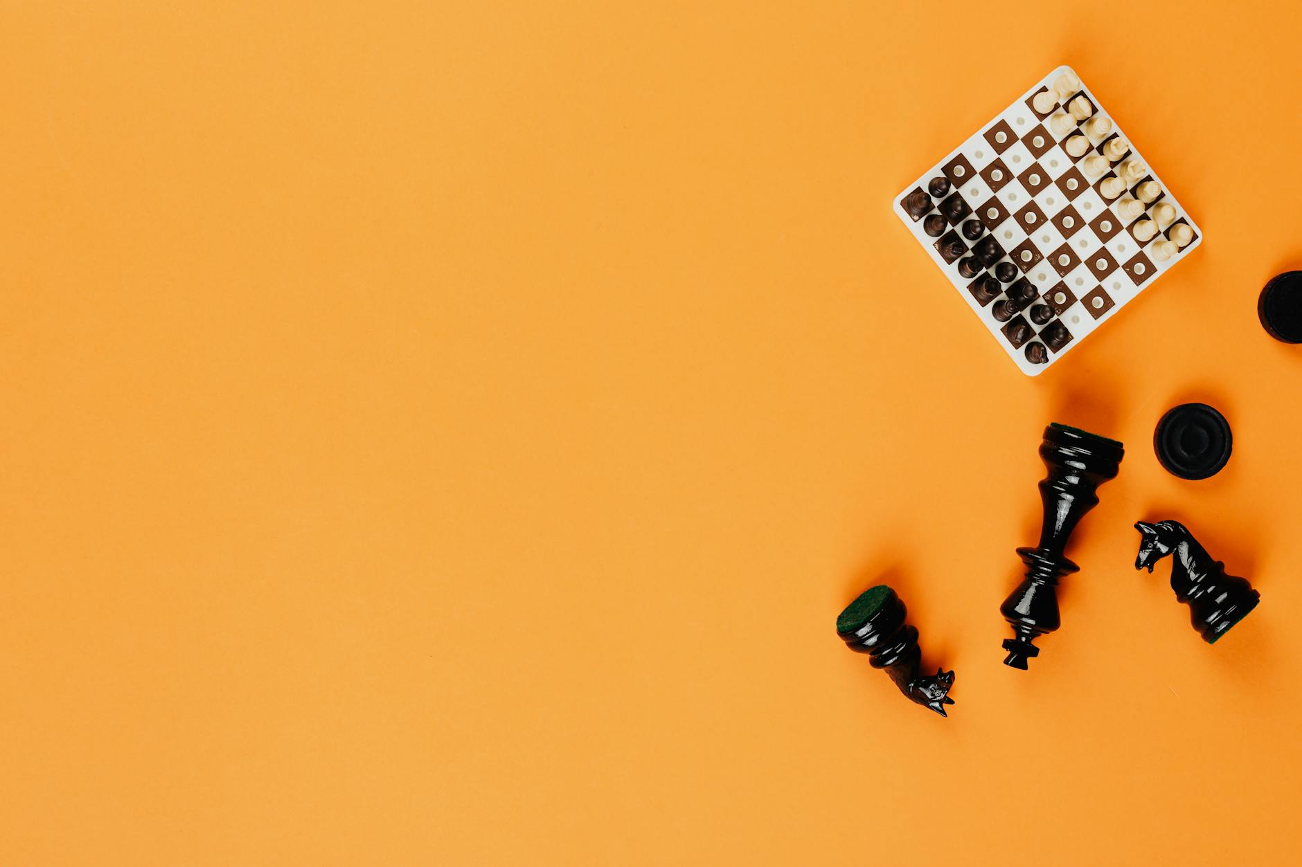 Flat lay of chess game pieces on a bright orange background with ample copy space.