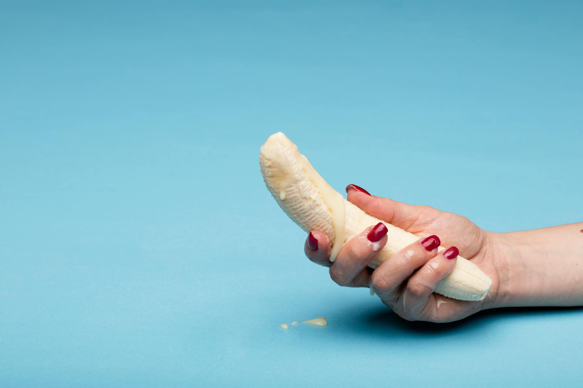Conceptual image of a hand holding a peeled banana on a blue background.