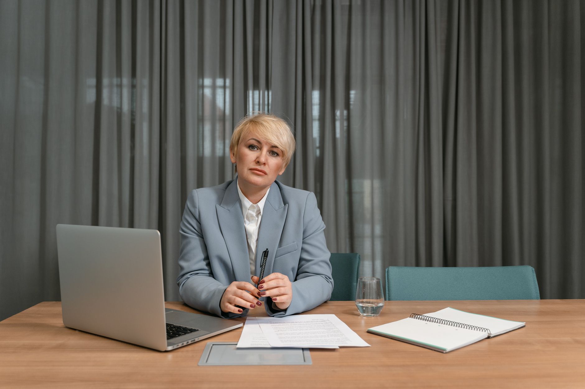 A confident businesswoman with short hair sits at a desk in a modern office environment.