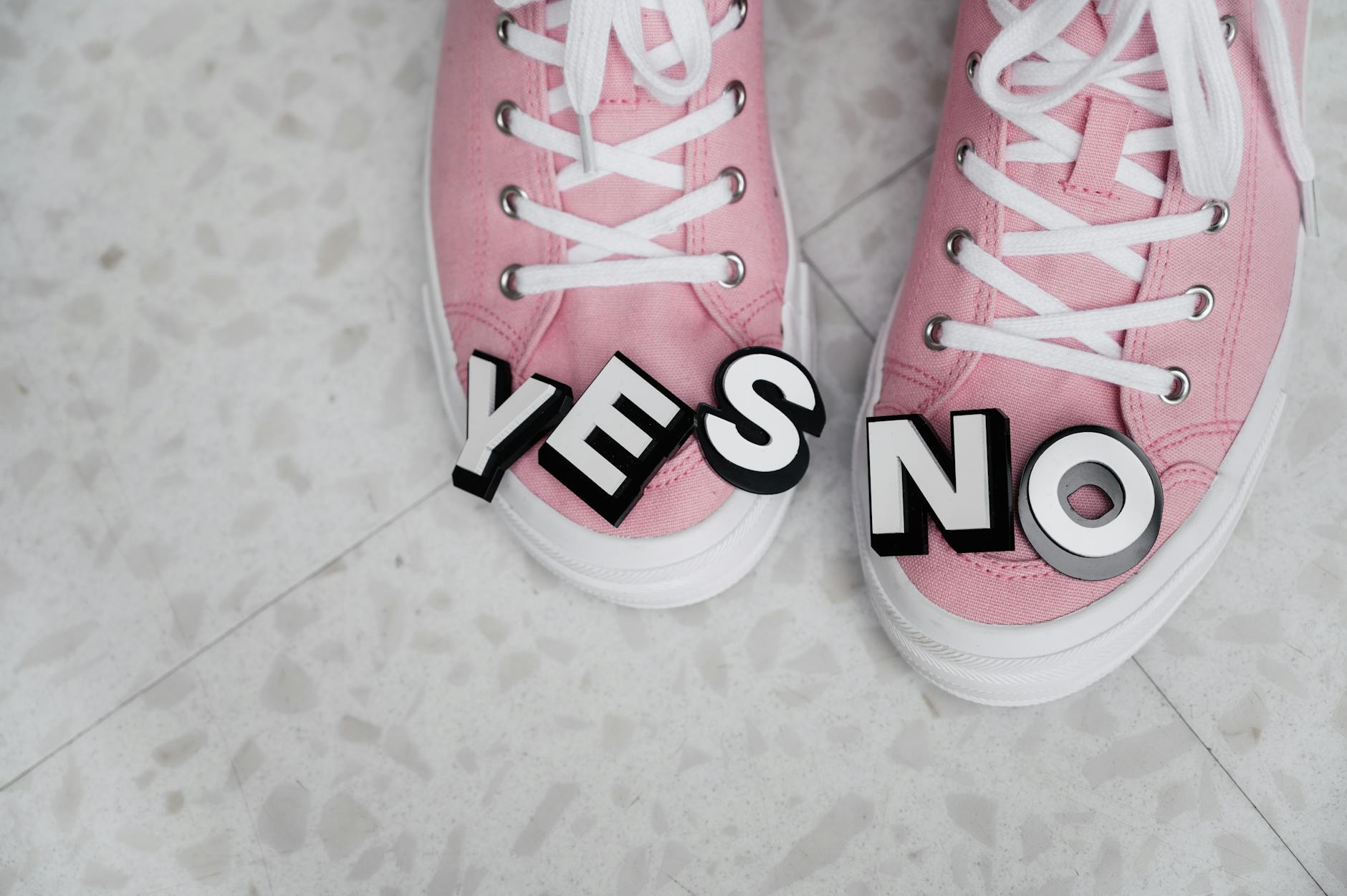 Pink sneakers with YES and NO letters on a tiled floor, symbolizing choice.