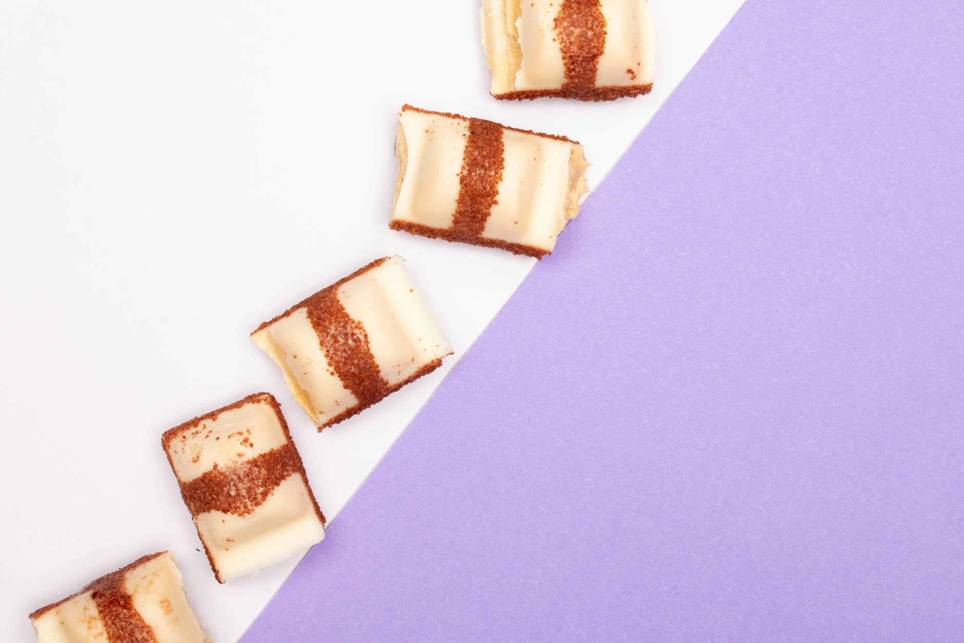 Five chocolate striped cream pastries on a minimalist white and purple background, top view.