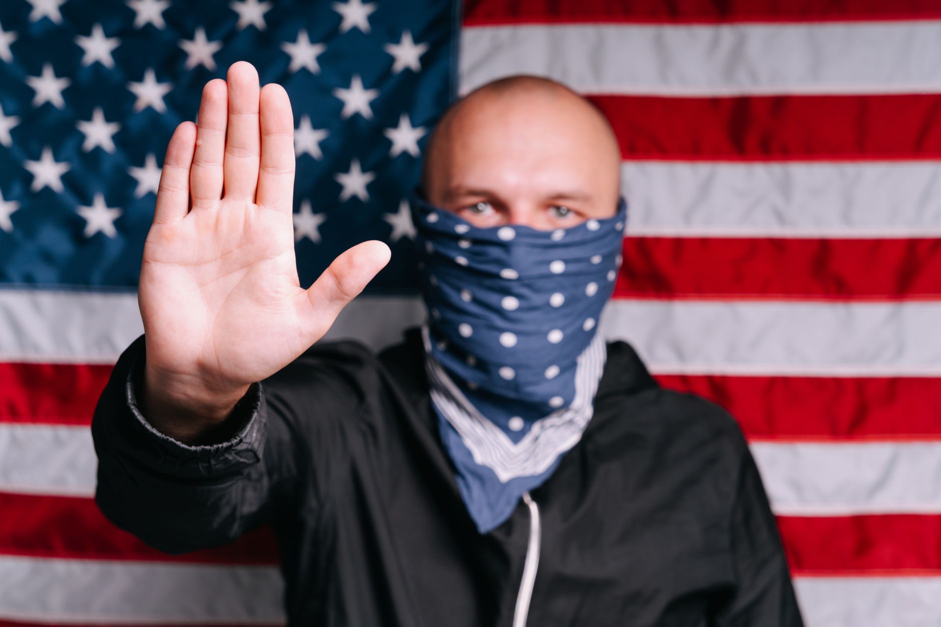 A masked protester gestures in front of an American flag, symbolizing activism.