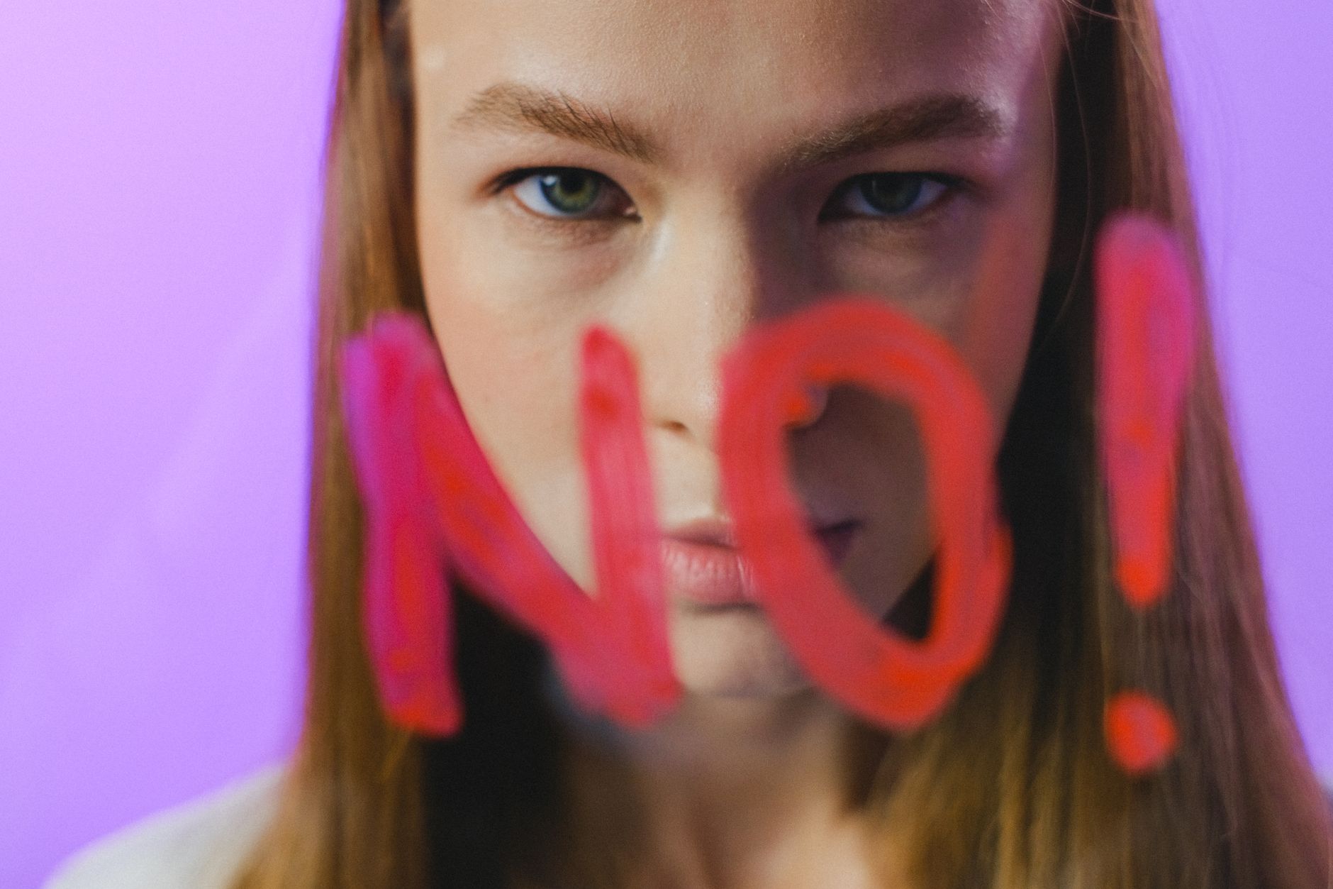 Teen girl with painted 'NO!' on glass, expressing refusal or disagreement in a studio setting.